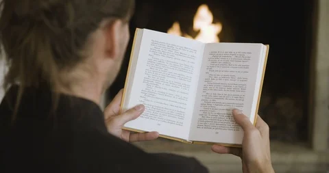 Reading a book in front of a fireplace closeup Stockbeeldmateriaal 97973710