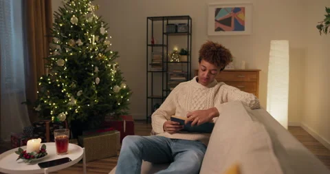 Reading a book by the lighted Christmas tree. A young man with curly hair Vidéo 210241416