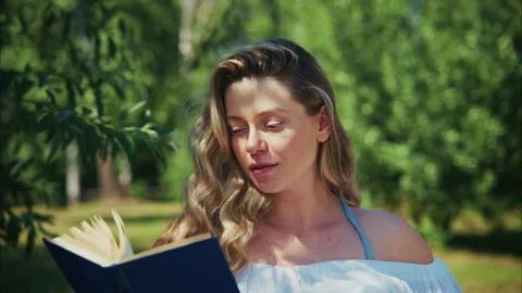 Reading a book in a serene garden setting on a sunny afternoon 스톡 동영상 312863157