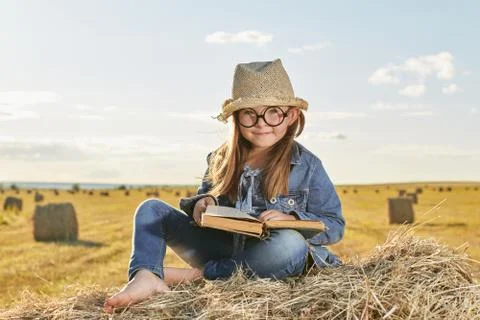Reading girl sits over the haystack roll on field in countryside Stock Photos