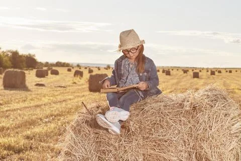 Reading girl sits over the haystack roll on field in countryside Stock Photos