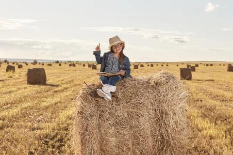 Reading girl sits over the haystack roll on field in countryside Stock Photos