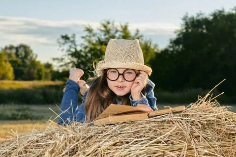 Reading girl sits over the haystack roll on field in countryside Stock Photos