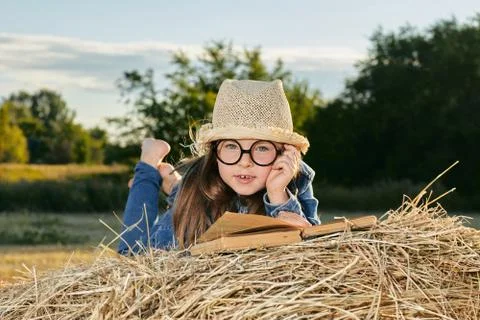 Reading girl sits over the haystack roll on field in countryside Stock Photos