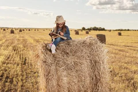 Reading girl sits over the haystack roll on field in countryside Stock Photos