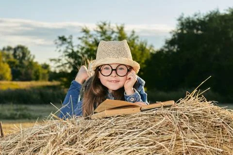 Reading girl sits over the haystack roll on field in countryside Stock Photos