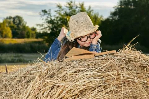 Reading girl sits over the haystack roll on field in countryside Stock Photos