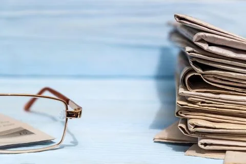 Reading glasses and stack of newspapers on a blue wooden shelf Stock Photos