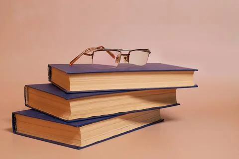 Reading glasses are on a stack of books on a colored background. Side view Stock Photos