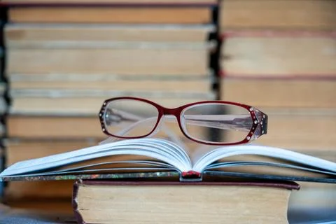 Reading glasses on book with stack of books in background. Stock Photos