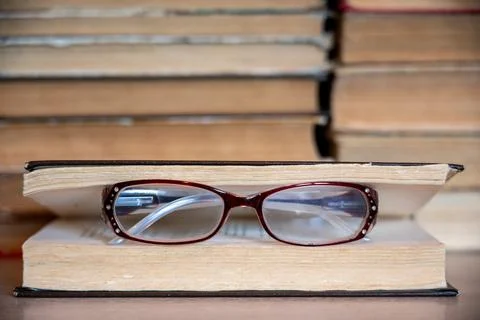 Reading glasses on book with stack of books in background. Stock Photos