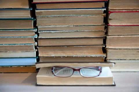 Reading glasses on book with stack of books in background. Stock Photos