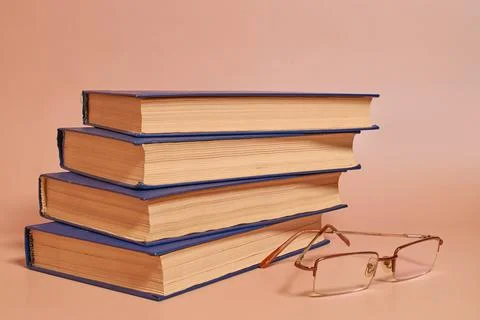Reading glasses lie next to a stack of books on a colored background. Side vi Stock Photos