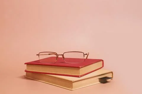 Reading glasses lie on a stack of old worn books on a colored background Stock Photos