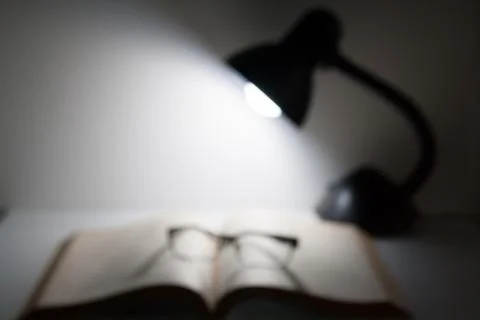 Reading glasses resting on top of open book next to night lamp Stock Photos