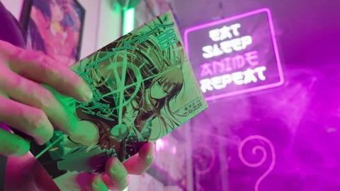 Reading Japanese manga comic under Eat Sleep Anime Repeat futuristic neon sign Stock Footage 320008717