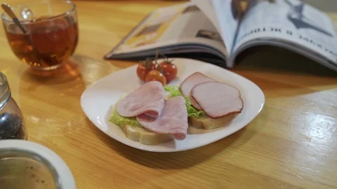 Reading magazine during breakfast in kitchen. Ham sandwich with tomatoes on 스톡 동영상 96194916