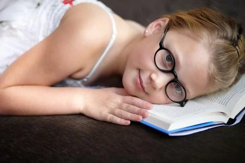 Reading myself to sleep. A young girl wearing glasses lying with her head on her Stock Photos