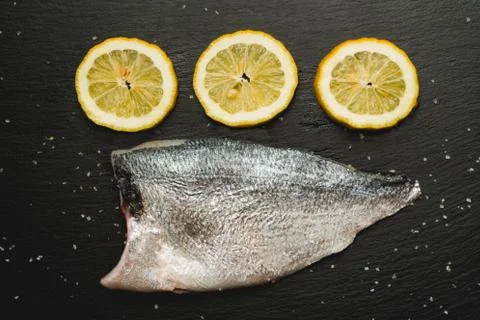 Ready to cook raw bream fish with lemon on black cutting board. Fotos Stock