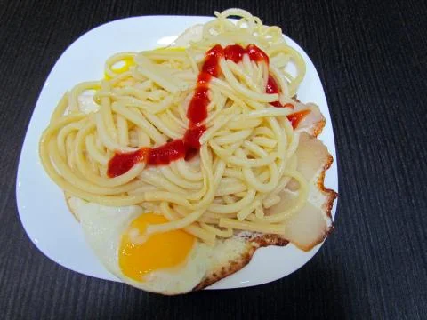 Ready dish which consists of spaghetti, fried eggs with bacon and ketchup Stock Photos
