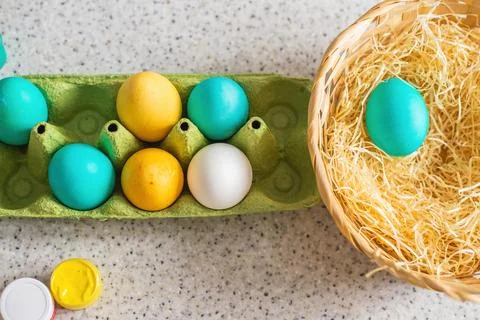 Ready-painted eggs stand on the table with paints and a wicker basket on a su Stock Photos