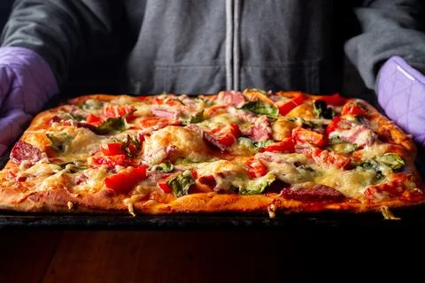 Ready pizza in hands on a baking sheet in hands in the kitchen at home. Stock Photos