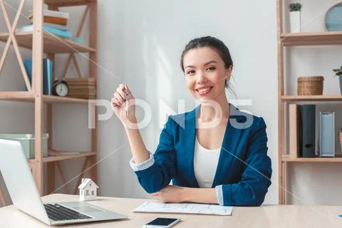 Real estate agent at agency sitting holding keys looking camera friendly Stock Photos