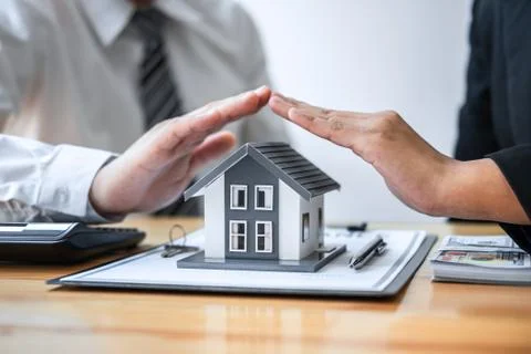 Real estate agent and customer covering Small house model and protection by h Stock Photos