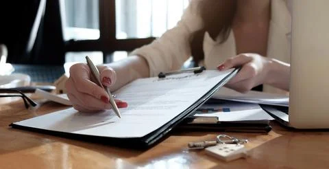 Real estate agent assisting client to sign contract paper at desk with hous.. Stock Photos