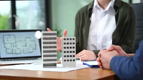 Real estate agent presenting floorplan to client with building models. Busi.. Stock Footage 312775227