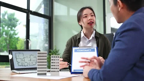 Real estate agent presenting floorplan to client with building models. Busi.. Stock Footage 312775241