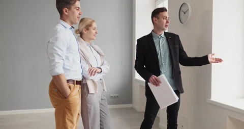 Real estate agent presenting spacious vacant apartment to interested couple Stock Footage 341801178
