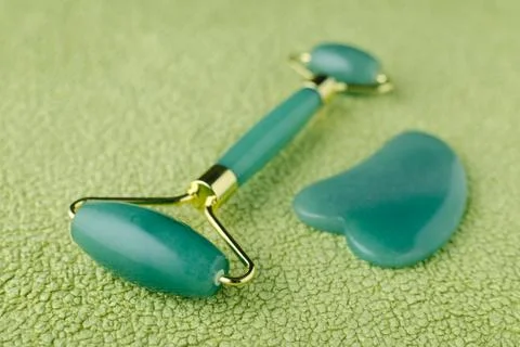 Real jade facial roller and massage stone gua sha on green background, closeup Stock Photos
