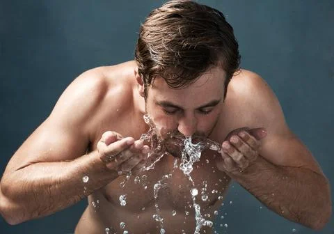 Real men take care of their skin. a young man washing his face against a grey Stock Photos