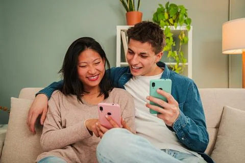 Real multiracial married couple using a cellphone to search apps sitting on Stock Photos