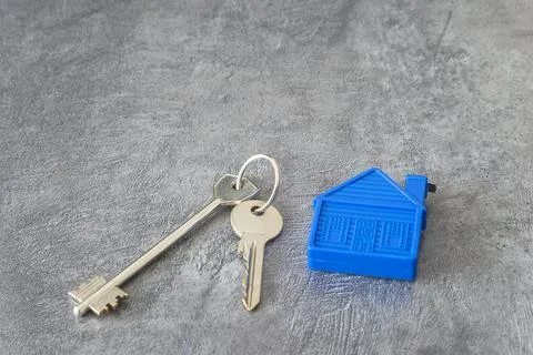 Real state concept; Two keys and blue house keychain on the gray textured b.. Stock Photos