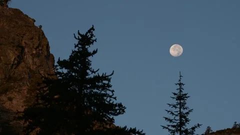 Real Time 4K Full Moon Setting Behind Mountain Peaks Under Blue Morning Sky Stock Footage 320011810