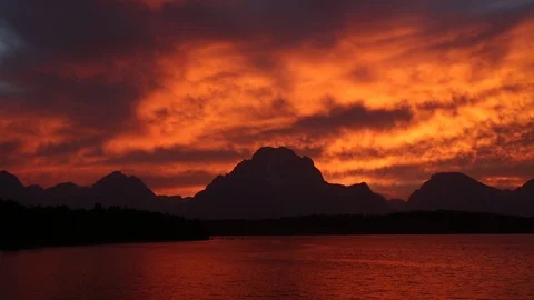 Real time of colorful sunset clouds above the Grand Teton mountains and a lake Stock Footage 95155177