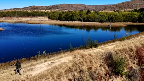Real time drone view of man clay pigeon shooting over remote farm dam Stock Footage 315653781