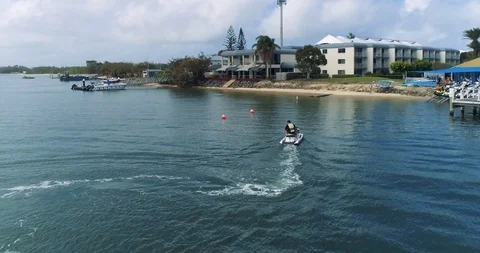 Real time fly with drone after jet ski watercraft parking at shore near hotel Stock Footage 99408613
