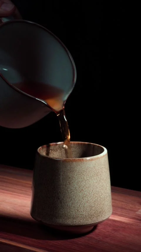 Real time hand pouring tea into ceramic cup dark background vertical Stock Footage 324762580