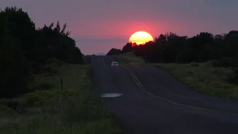 Real time long shot of a lone car driving off into the sunset in Arizona Stock Footage 160625196