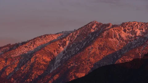 Real time long shot of pink sunset sunlight illuminating a snowy mountain 스톡 동영상 136862229