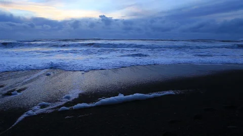 Real time, low angle view of blue sunset clouds reflected in approaching waves Stock Footage 130273215