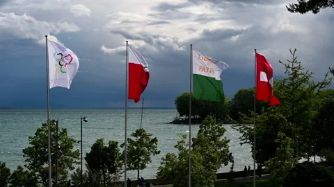 Real time of Olympic, Cantonal and Swiss Flags Flying over Lake Geneva in Windy Stock Footage 336576014