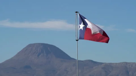 Real time shot of a Texas state flag waving in blue sky and a desert hill Stock Footage 166875904