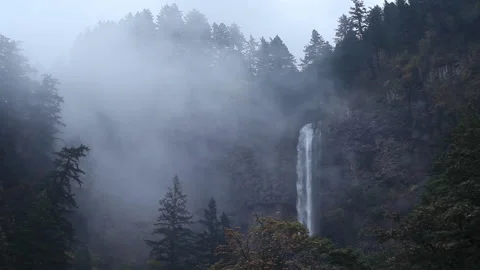Real time view of fog drifting around a forested ridge and Multnomah Falls Stock Footage 132004113