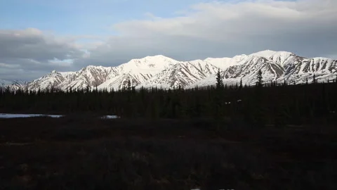 Real time view of sunset cloud shadows on snowy mountains and Alaskan forest Stock Footage 242982559
