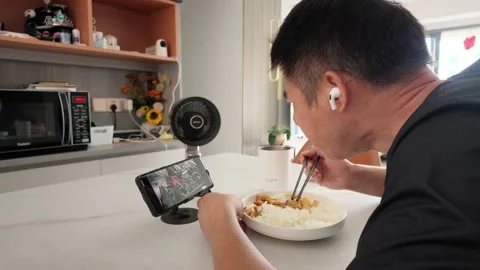 Real-world video: Man Eating Rice Watching Phone With Earbuds In Kitchen Vídeos de archivo 343367994