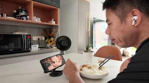 Real-world video: Man Eating Rice Watching Phone With Earbuds At Table Vídeos de archivo 343368712